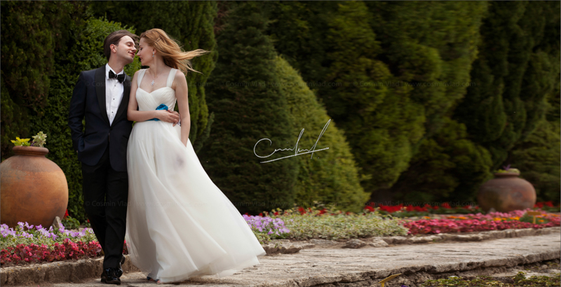 Bride and groom walking on a road surrounded by flowers with the wind in their hair