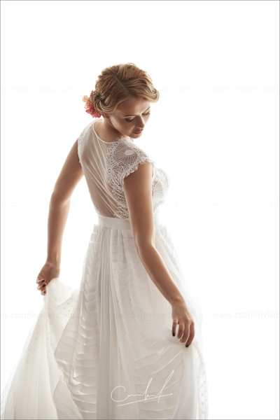 White background image of bride with hair gathered in a low bun and wearing a pink flower as hair accesory